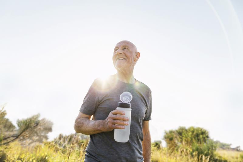 An older man takes a water break during a sunny outdoor hike