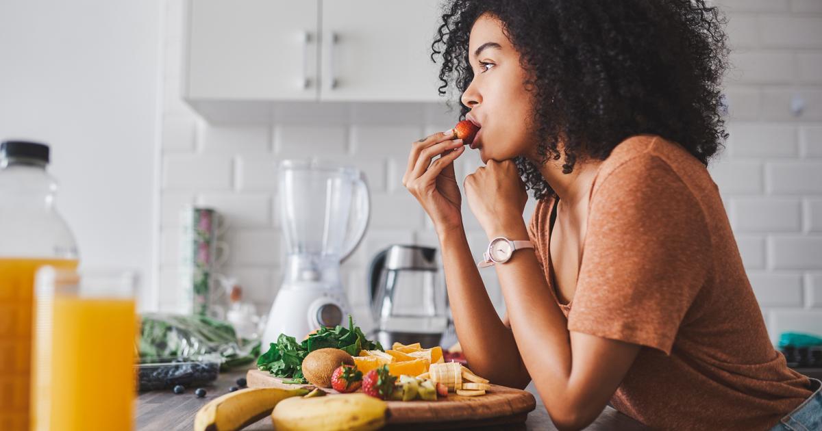 woman in her kitchen eating healthy fruits and vegetables woman in her kitchen eating healthy fruits and vegetables