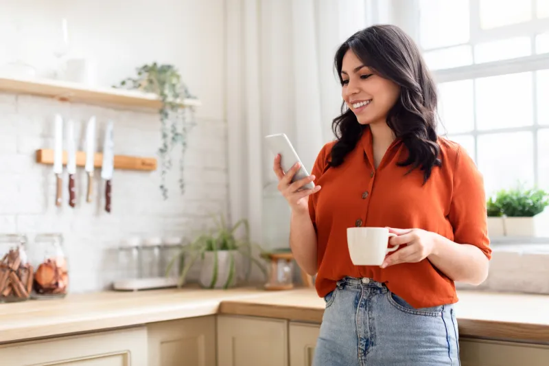 Younger woman using her phone in her kitchen