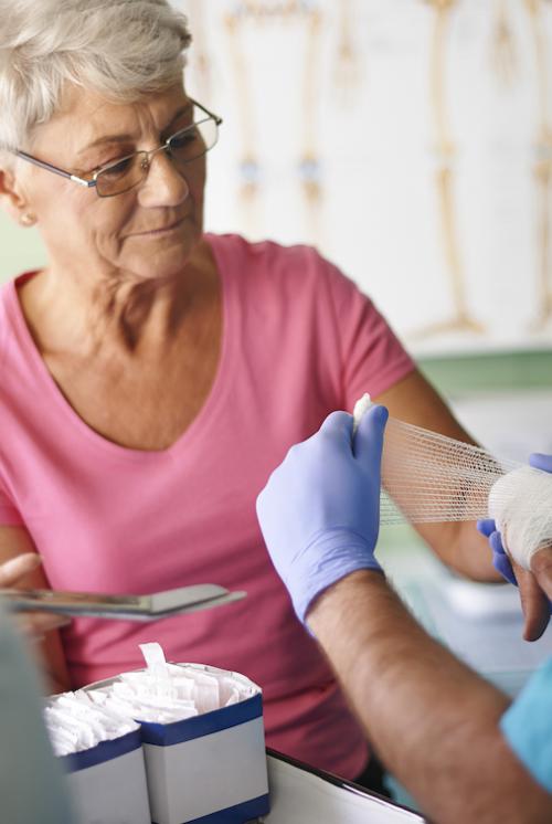 An older woman has her hand bandaged by a nurse